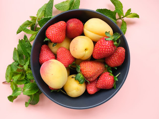 Red ripe strawberries and fresh apricot in bowl decorated mint leaves on pink background. Ingredients for summer vitamin refreshing cocktail or smoothie. Healthy natural fruit  and  berry dessert. 
