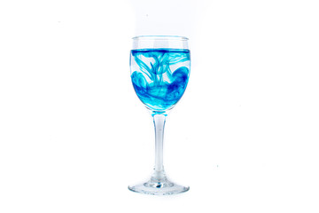 Blue food coloring diffuse in water inside wine glass with empty copyspace area for slogan or advertising text message, over isolated white background.
