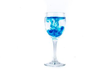 Blue food coloring diffuse in water inside wine glass with empty copyspace area for slogan or advertising text message, over isolated white background.