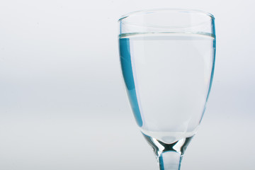 Blue food coloring diffuse in water inside wine glass with empty copyspace area for slogan or advertising text message, over isolated white background.