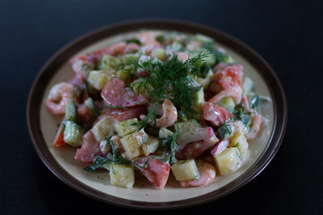 Homemade salad with shrimps and fresh vegetables sauced with yogurt decorated with fennel on plate on black table