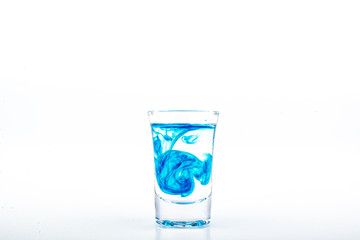 Blue food coloring diffuse in water inside shot glass with empty copyspace area for slogan or advertising text message, over isolated white background.