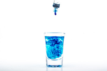 Blue food coloring diffuse in water inside shot glass with empty copyspace area for slogan or advertising text message, over isolated white background.