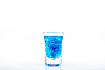 Blue food coloring diffuse in water inside shot glass with empty copyspace area for slogan or advertising text message, over isolated white background.