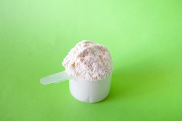 WHEY protein powder with plastic spoon on green background