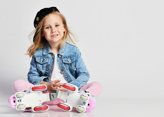 girl sits on the rollers in a blue denim and cap and smiles. Summer sports for children.