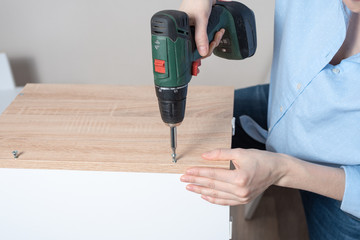 Female hands closeup with a cordless driver collects furniture