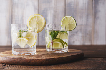 Two glasses of homemade summer refreshing lemonade on a wooden Board with lemon, mint and ice