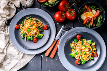 Italian pasta with vegetables and salad with arugula and mozzarella on a dark wooden background. Traditional Mediterranean cuisine. Vertical shot