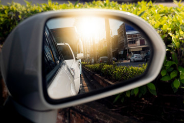 Cars run through the street from the White car's side view mirror. with tree and city beside.