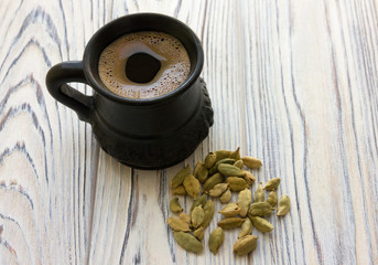 Arabic coffee in black ceramic cup and cardamom granules on light gray wooden background.