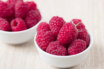 Fresh raspberries in white ceramic cup on white rustic wooden background with copy spice