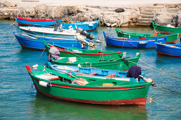 Fototapeta na wymiar Beautiful old colored fishing wooden boats on the water with rocks on background