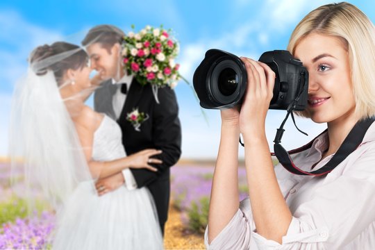 Female photographer holding camera and just married couple on background