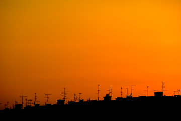 Fototapeta na wymiar city silhouette with roofs and antennas against orange sky