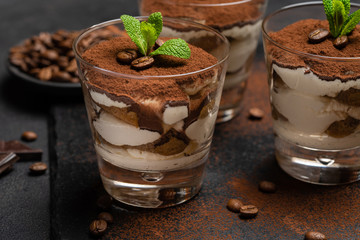 Classic tiramisu dessert in a glass on stone serving board on dark concrete background