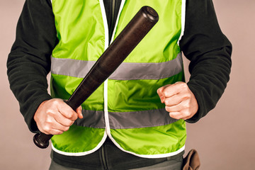 man in a yellow vest, a Builder or a protester with a baseball bat in his hands on a gray background