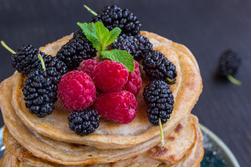 Delicious pancake with blackberries, raspberries and icing sugar in dish on black table.
