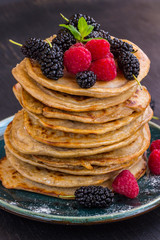 Delicious pancake with blackberries, raspberries and icing sugar in dish on black table.