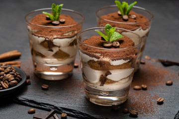 Classic tiramisu dessert in a glass on stone serving board on dark concrete background