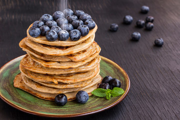 Delicious pancake with blгуberries, and icing sugar in green dish on black table.