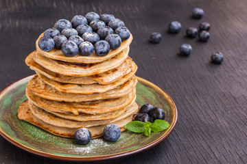 Delicious pancake with blгуberries, and icing sugar in green dish on black table.