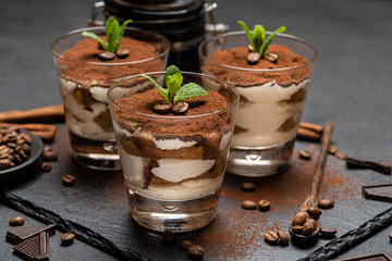 Classic tiramisu dessert in a glass on stone serving board on dark concrete background
