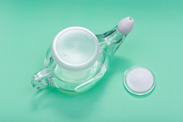 Neti Pot with Soft Comfort Tip and pile of saline (sodium bicarbonate and sodium chloride) on green background. Sinus wash. Nasal irrigation.