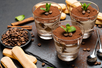 Classic tiramisu dessert in a glass and savoiardi cookies on stone serving board on dark concrete background