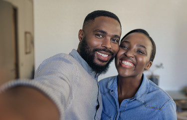Smiling young African American couple taking selfies at home