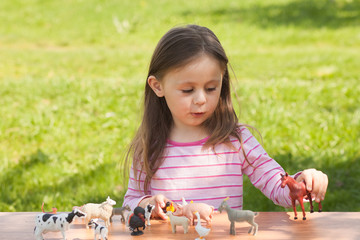 Cute toddler girl playing with farm animal figures outdoors. Summer leisure. childhood on countryside. Child learning farm animals. Early education and development