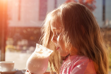 Little girl drinks milk cocktail in a cafe