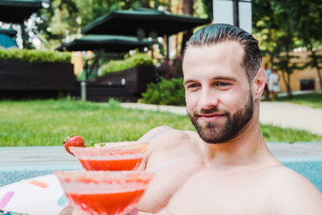 handsome bearded man smiling while looking at red cocktail