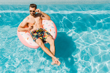 overhead view of handsome man touching sunglasses and holding cocktail glass
