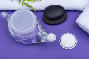 Spa purple background with Neti Pot, pile of Saline, rolled up White Towels and stacked Basalt Stones. Sinus wash. Nasal irrigation.