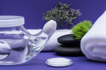 Obraz na płótnie Canvas Spa purple background with Neti Pot, pile of Saline, rolled up White Towels and stacked Basalt Stones. Sinus wash. Nasal irrigation.