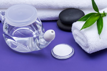 Spa purple background with Neti Pot, pile of Saline, rolled up White Towels, stacked Basalt Stones and Bamboo Leaves. Sinus wash. Nasal irrigation.