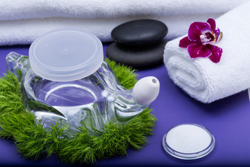 Obraz na płótnie Canvas Spa purple background with Neti Pot, pile of Saline, rolled up White Towels, stacked Basalt Stones and Orchid Flower. Sinus wash. Nasal irrigation.