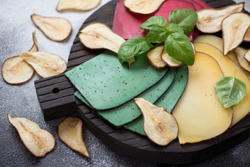 Assortment of cheese with pear chips and fresh green basil on a black wooden serving board, close-up