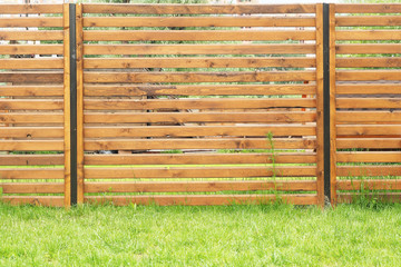 Background and texture of the fence of wooden planks covered with wood stain and green lawn..