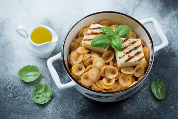 Bowl of orecchiette with sun dried tomato pesto and grilled cheese, high angle view on a grey stone background