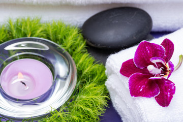 Wellness Relax concept with Spa elements. White Towels, Basalt Stones, Orchid, Lavender Tea Light Candle and Dianthus Flowers on purple background.