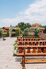 Stylish open space for a European wedding ceremony with wooden benches and a handmade arch. The arch is decorated with yellow flowers in the summer.