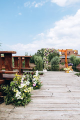 Stylish open space for a European wedding ceremony with wooden benches and a handmade arch. The arch is decorated with yellow flowers in the summer.