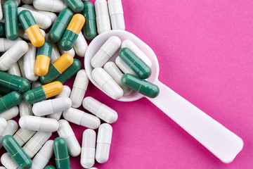 Plastic spoon and green, yellow and white pills on pink background