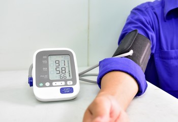 The doctor used a blood pressure monitor to measure the blood pressure of the worker before he started working. He wearing a blue uniform and sitting on the chair on the white background.
