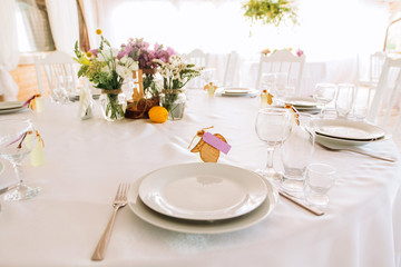 Table served for special occasion. Empty plate, glasses, forks, napkin and flowers on table covered with white tableclothes. Elegant dinner table. White table setting