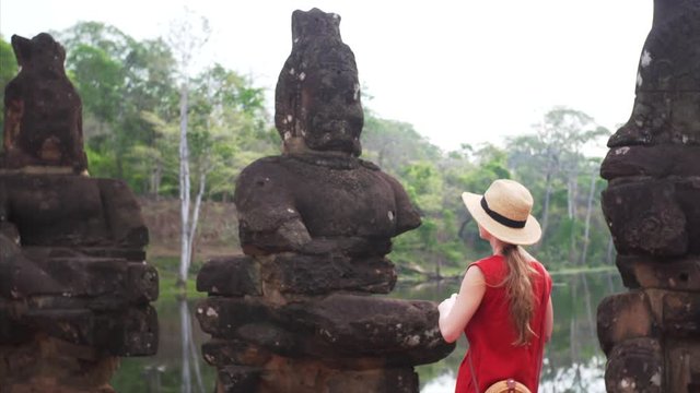Female tourist is taking pictures of asuras and devas statues on bridge to Angkor Thom temple in Cambodia. 