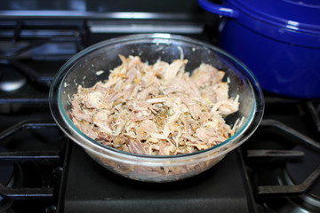 Delicious roasted pulled pork in a glass bowl on the stove top in a home kitchen.