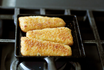 Fish sticks baked on a raclette pan resting on the stove top.